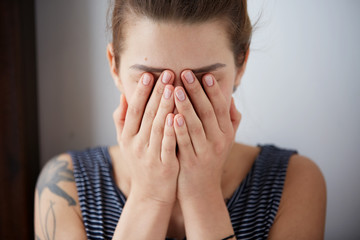 Frustrated stressed young woman. Headshot unhappy overwhelmed girl having headache bad day keeps hands on face out isolated on wall background. Negative emotion face expression feelings perception.