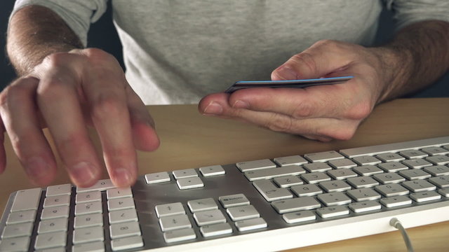 Man making online internet payment transaction using credit card, typing account number on desktop computer keyboard.