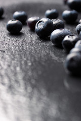 Closeup of fresh ripe blueberries on a black stone background with copy space, vertical, selective focus.