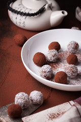 Chocolate sweets with cocoa and coconut chips on a white plate, selective focus.