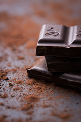 Dark chocolate stack with cocoa powder on a stone background, closeup, selective focus..
