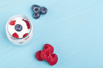 Glass of yogurt with berries and blueberries on a turquoise wood