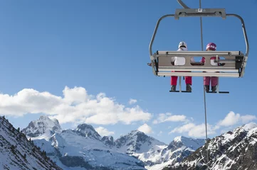 Poster Chairlift full of skiers at a ski resort with snowy mountains on background © cmassway