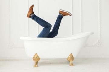 Feet in jeans and gym shoes looking out of a white bath in a whi