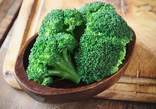 Bunch of fresh green broccoli on brown plate over wooden background