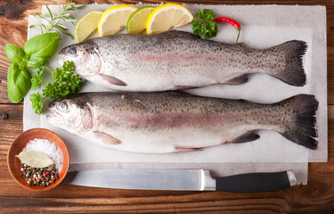 Two rainbow trout on a board, with herbs and peppercorns, ready for cooking.