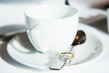 Cup of coffee, wedding rings in spoon on table