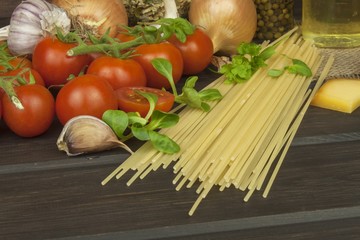 Preparing homemade pasta. Pasta and vegetables on a wooden table. Dietary food. Pasta, tomatoes, onion, olive oil and basil on wooden background. 
