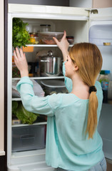  long-haired woman arranging space in fridge at home