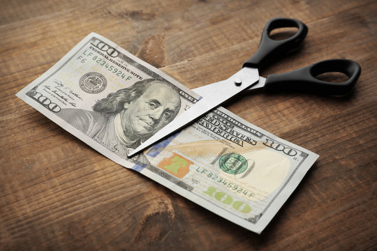 Scissors cuts dollar banknote on wooden background