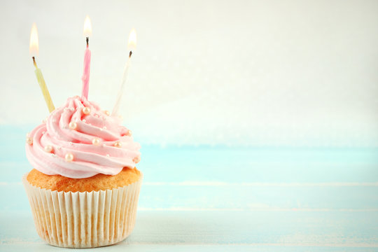 Tasty pink cupcakes decorated with candles on light background