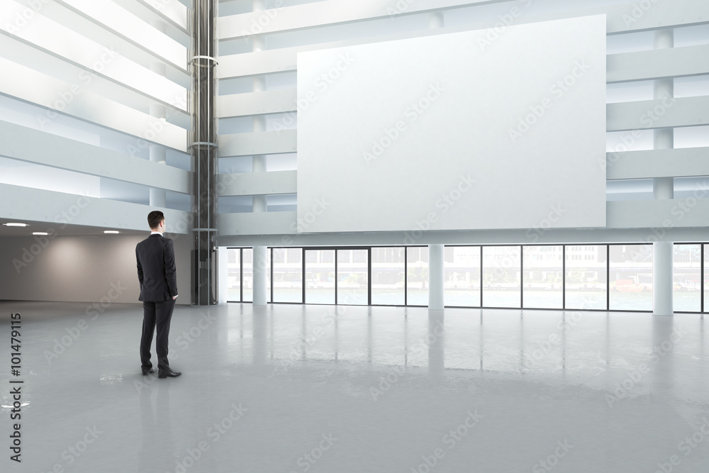 Poster man looking at a blank white banner in a large bright hall, mock