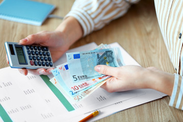 Woman counting money and working on  calculator at the table
