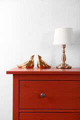 Room interior with red wooden commode and lamp on light wall background