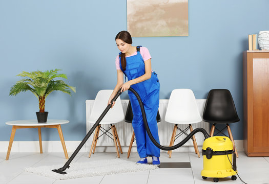 A Pretty Young Woman In Uniform Vacuuming The Floor At The Office