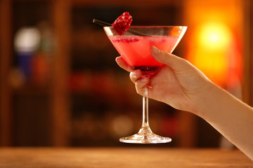 Female hand with glass of cocktail on bar background