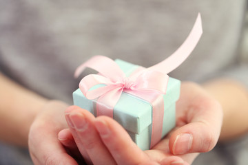 Female hands holding beautiful small gift wrapped with satin ribbon.