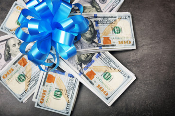 Pile of dollars with bow as gift on grey textured background