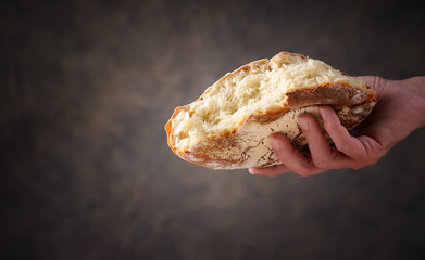 Hand giving a piece of bread on dark background, space for text.