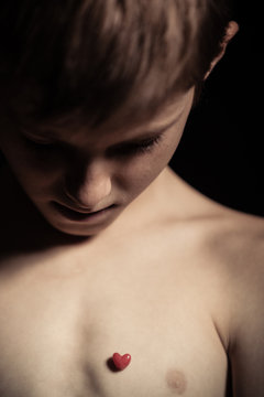 Young boy looking at a tiny red heart on his chest