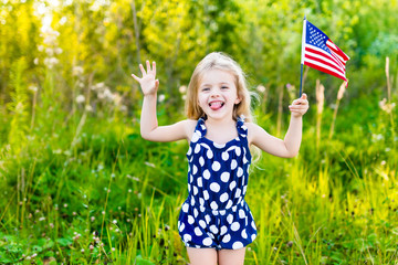 Funny little girl with long curly blond hair putting out her tongue and waving american flag,...