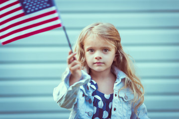Adorable little girl with long curly blond hair holding american flag and waving it. Independence Day, Flag Day concept. Vintage and toning