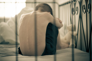 Maltreated Boy Sitting on Bed and Hiding his Face