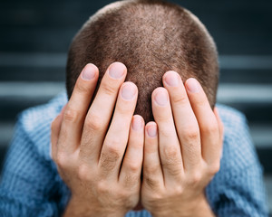 Closeup portrait of despaired young man covering his face with hands. Selective focus on hands....