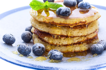 Pile of pancakes with blueberries sprinkled with icing sugar and honey