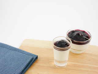 The tasty homemade blueberry panna cotta (Italian pudding dessert) in the small glass and blue cotton fabric on wooden board.