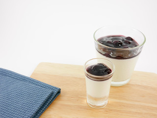 The tasty homemade blueberry panna cotta (Italian pudding dessert) in the small glass and blue cotton fabric on wooden board.