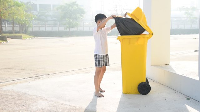Young Asian boy looking to the yellow bing and take black plastic garbage bag
