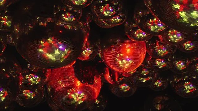 Mirror balls reflect rays of colored lights. Colorful reflective disco mirror ball with glinting highlights spinning slowly on a blurry colored background in disco club. The light show at night.