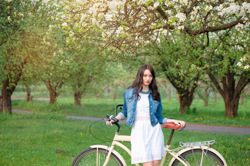 Fototapeta na wymiar Week end in spring park. Attractive young brunette woman walking with a bicycle against nature background.