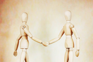 Two men shake hands to each other. Abstract image with wooden puppets