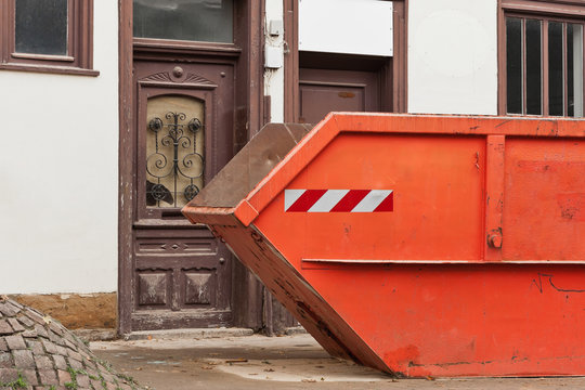 Ein grosser oranger Container für Abfall vor einem alten Haus