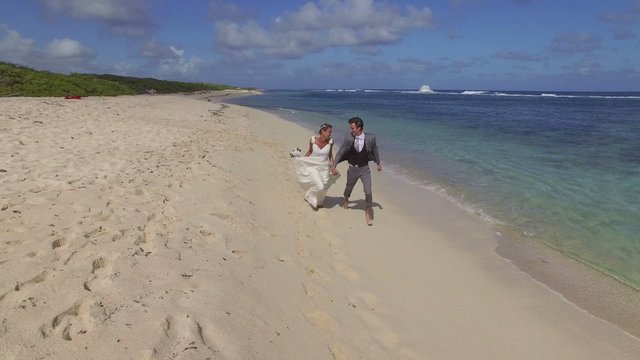 Bride and groom running on a sandy beach