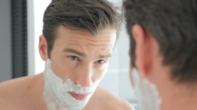 Adult man shaving with foam and manual razer