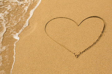 Heart drawn on the beach sand with a soft wave.
