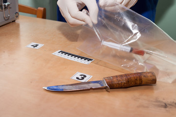expert inspects a syringe with blood and a knife at the crime scene