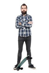 Proud hipster wearing tartan plaid shirt standing on skateboard with crossed arms. Full body length...