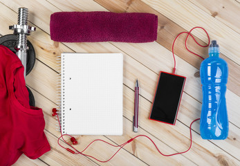 Sport Equipment. Barbell, Red Shirt, Isotonic Drink, Towel, Smart Phone With Earphones And Notebook To Workout Plan On Wooden Table. Sport Fitness Background