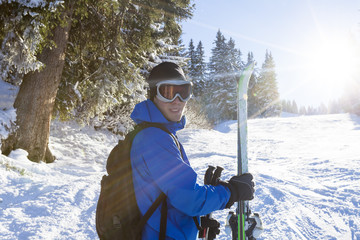 Smiling skier standing near the forest with ski in hand
