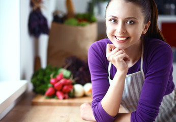 Young woman standing in her kitchen near desk