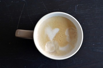 brown white coffee cup with coffee cream in heart shape on a old black wooden table with empty copy space
