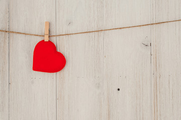 Red heart hanging on the clothesline. On old wood background