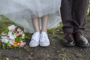 the couple stand on grass. Bride in sneakers