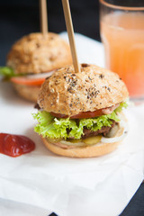 Fresh homemade burgers on wooden cutting board over dark background.