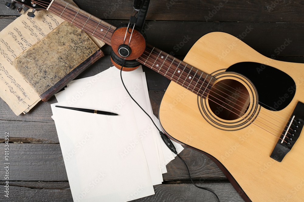 Poster acoustic guitar, headphones, musical notes and white papers on wooden background, close up