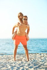 A guy carrying a girl on his back, at the beach, outdoors